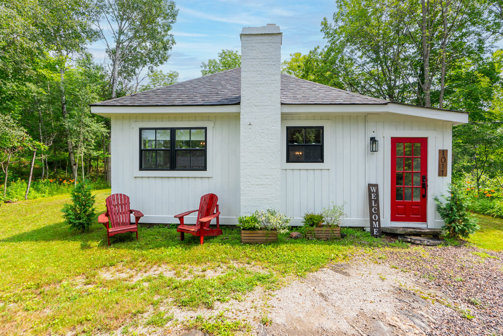 A small white house with a red door in a rural area.