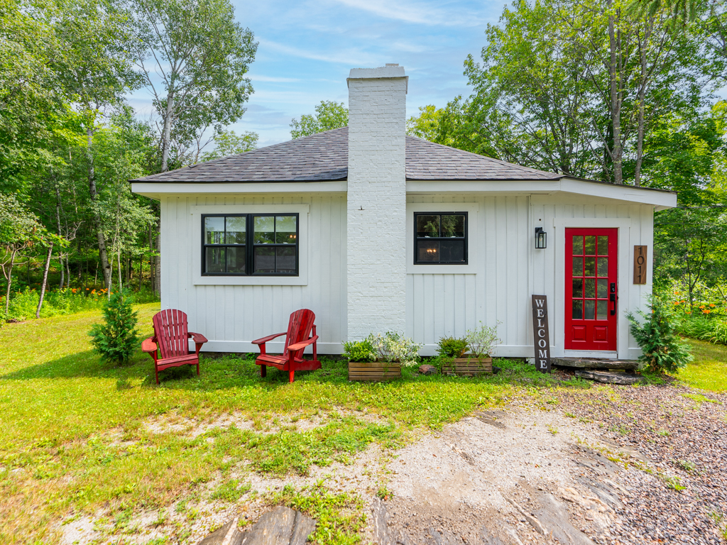 A small white house with a red door in a rural area.