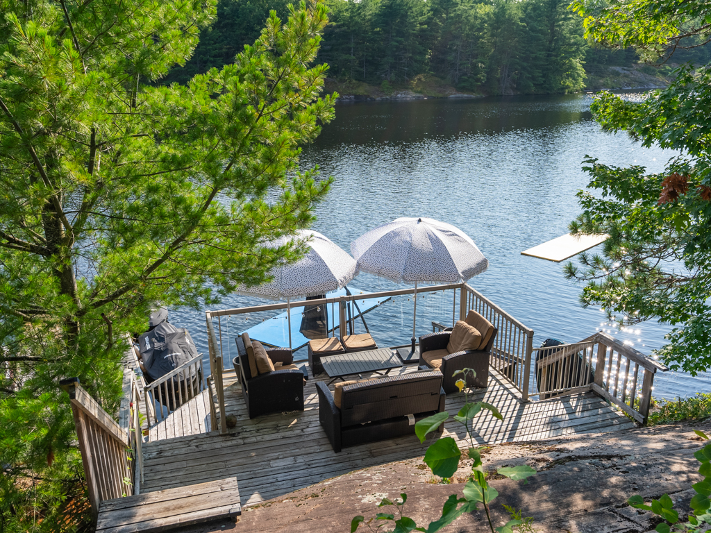 Looking down from one deck to another deck, which is closer to the lake and has a table, chairs, and umbrellas.