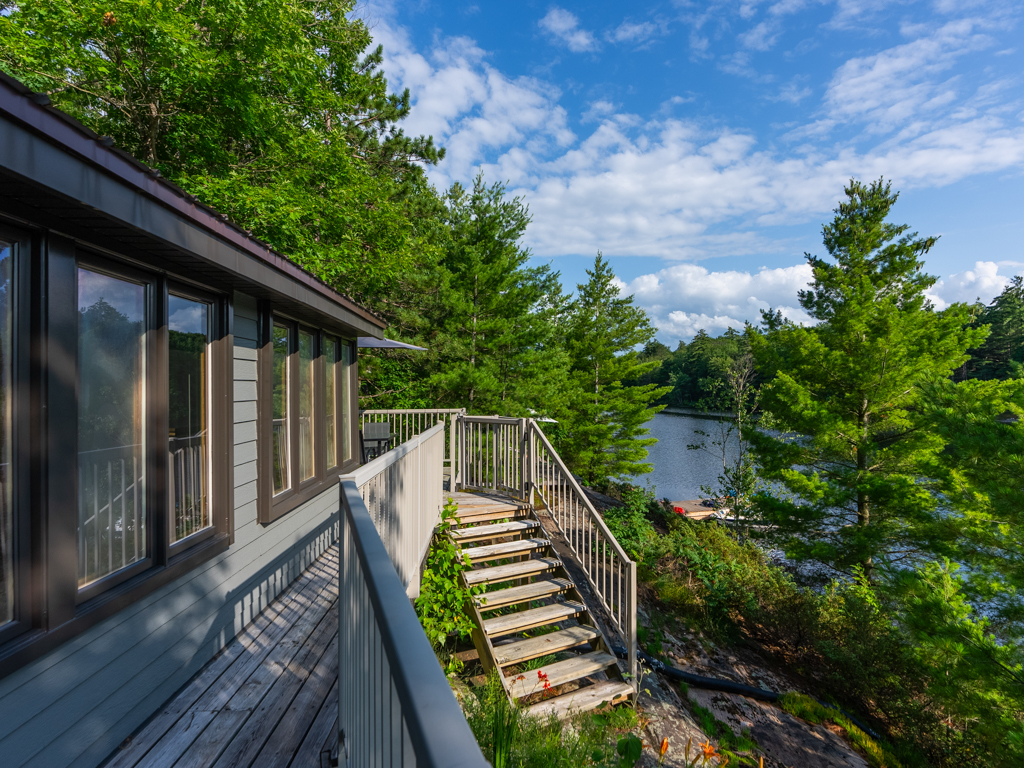 A narrow stretch of deck off the back of a cottage, leading to stairs down to the lake.