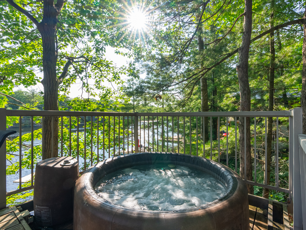 A round hot tub on the deck of a cottage, surrounded by trees on the other side.