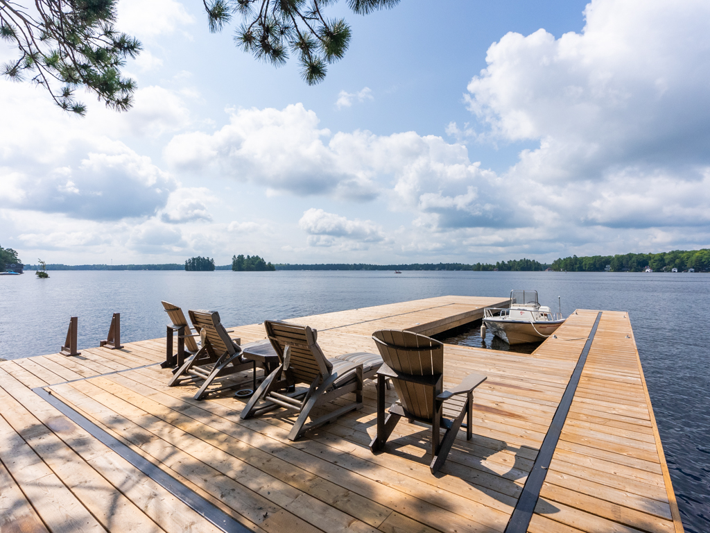 Four lounger chairs sit on a big, new dock, which extends out into a lake.