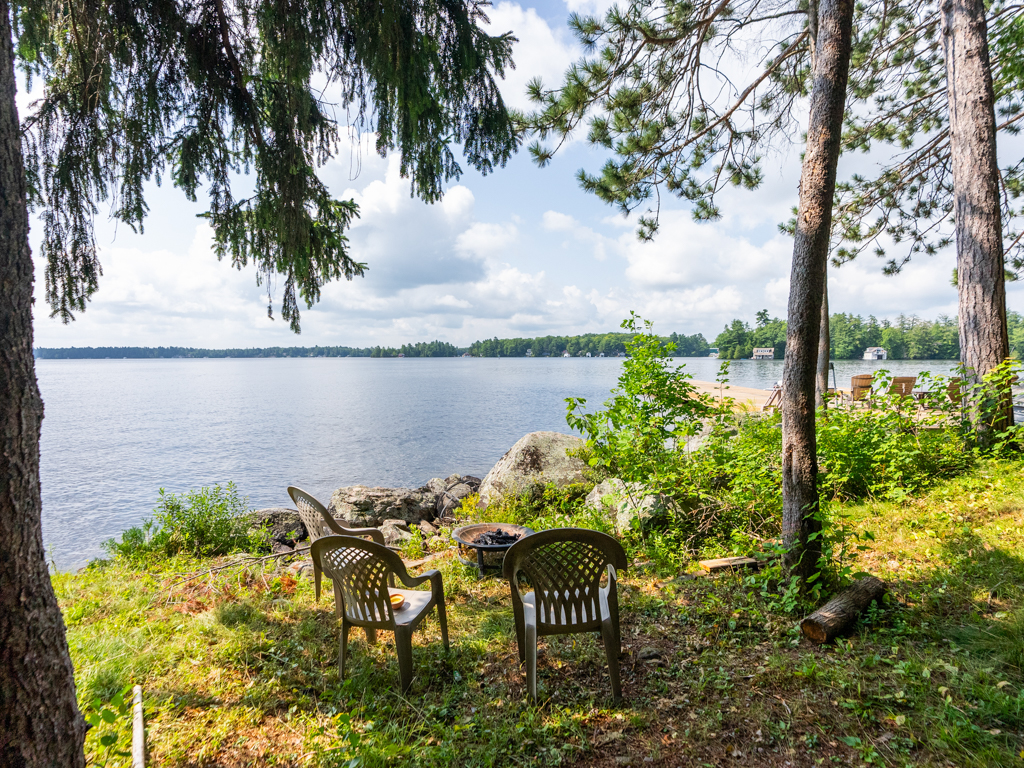 Chairs sit around a small fire pit on the shore of a lake.