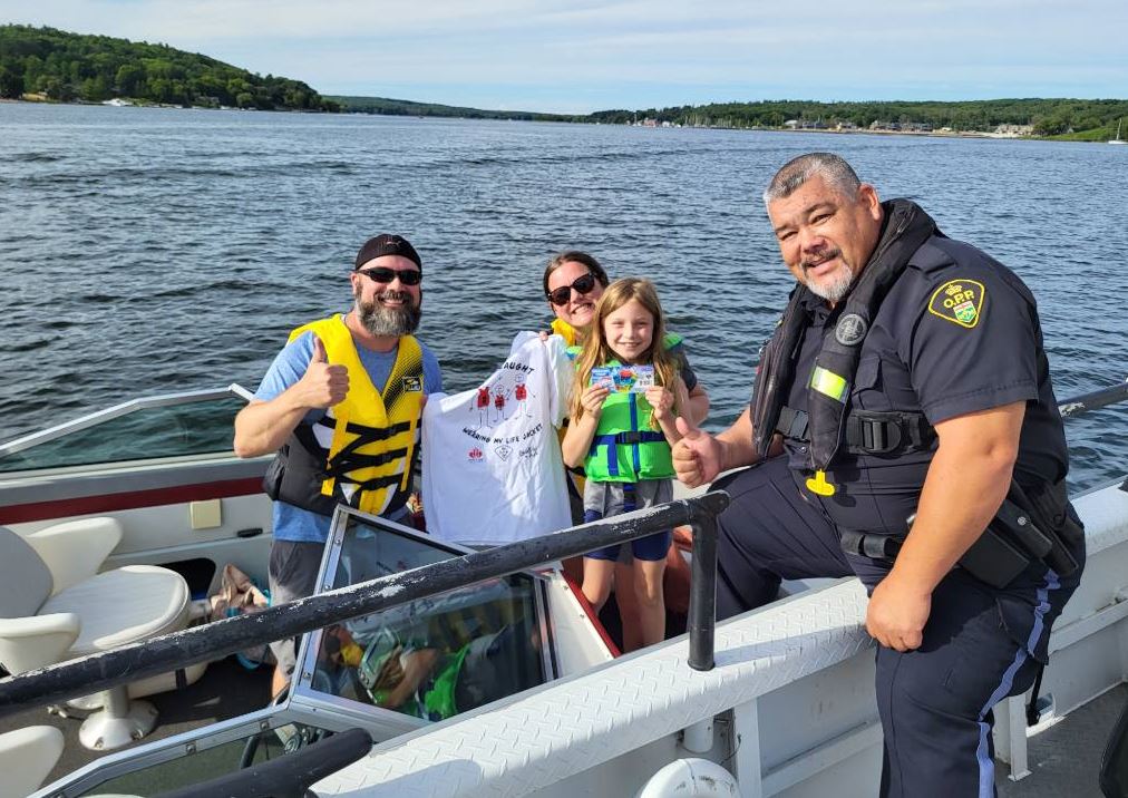 OPP officer posing with family receiving "I got caught wearing my lifejacket" shirt