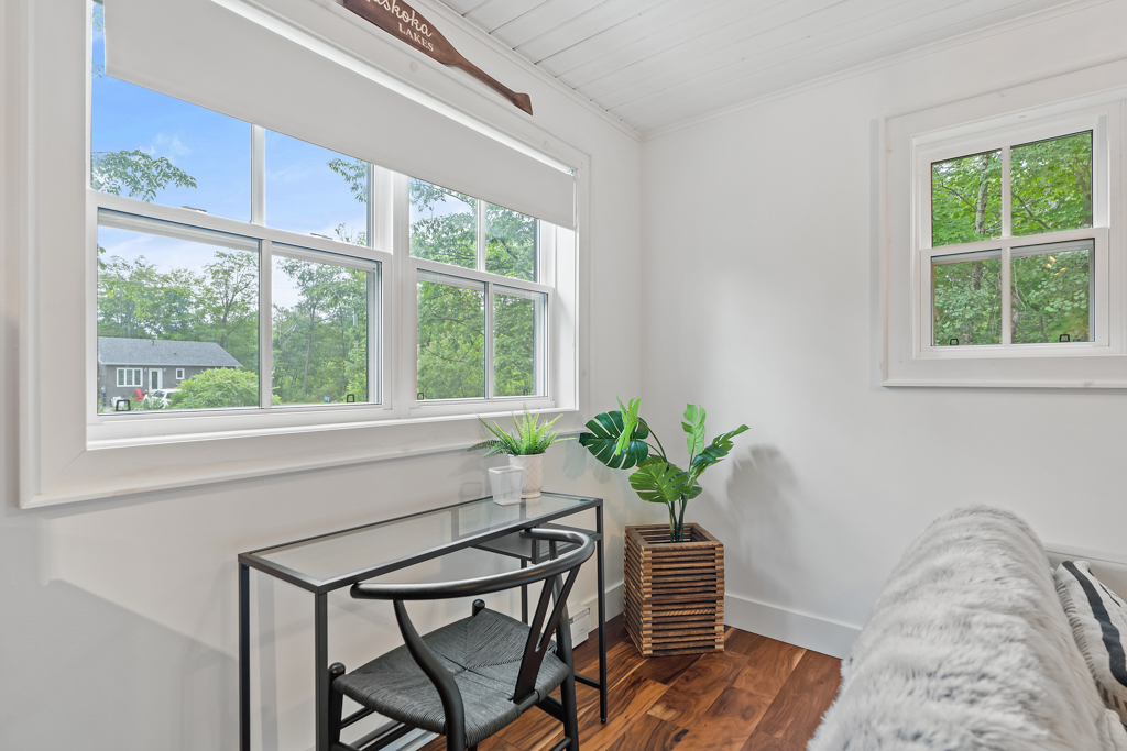 A small glass table and a chair sit under a window.