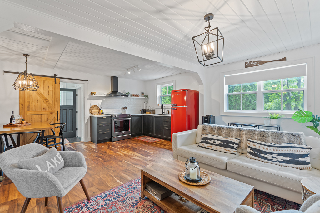 A bright, open-concept space with hardwood floors, a small living area, and a modern kitchen with a red fridge.