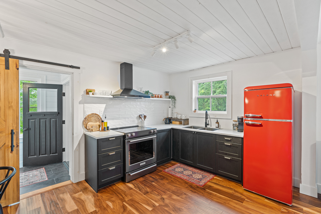 An updated kitchen with black cabinets and a red fridge sits just inside the entrance of a small house.