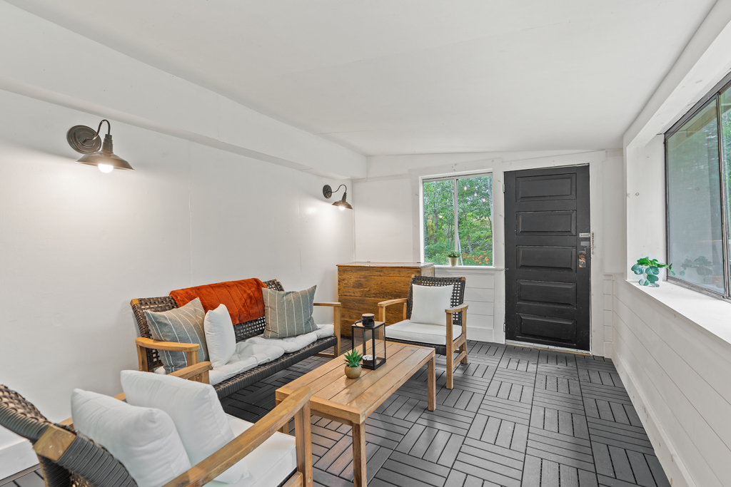 A bright sunroom sitting area with chairs, a couch, and lots of windows. A door leads to outside.