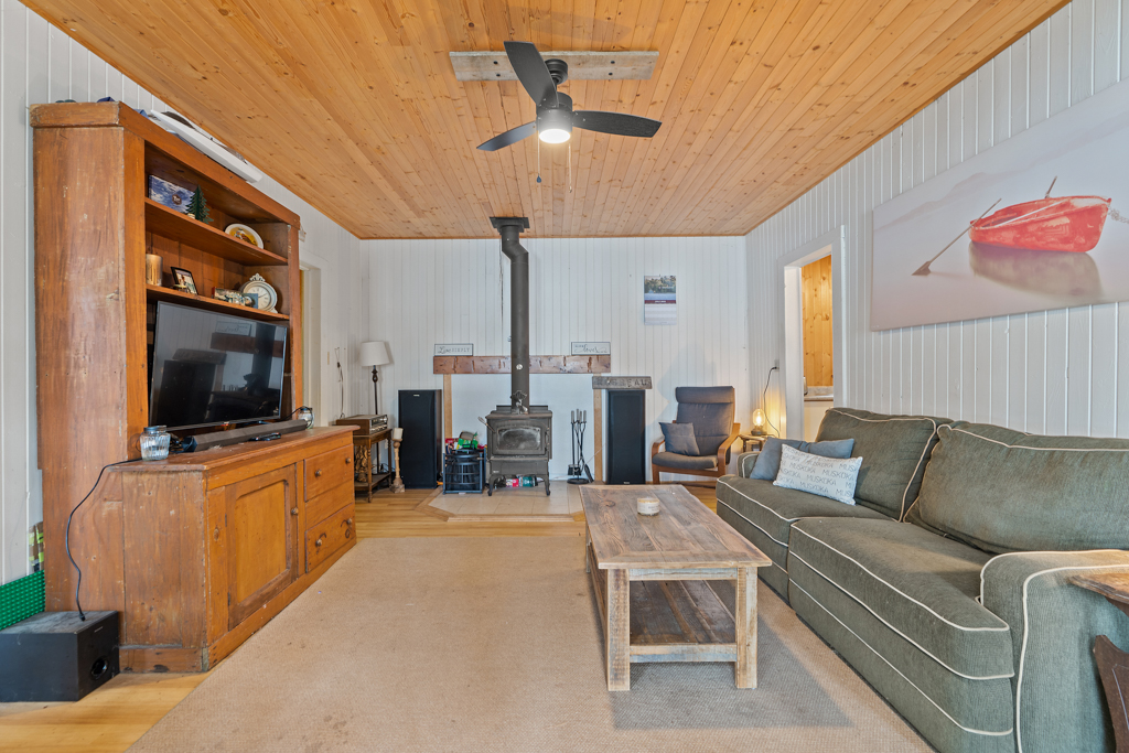 A bright, open cottage living space with a television, a couch, a coffee table, and a wood-burning fireplace.