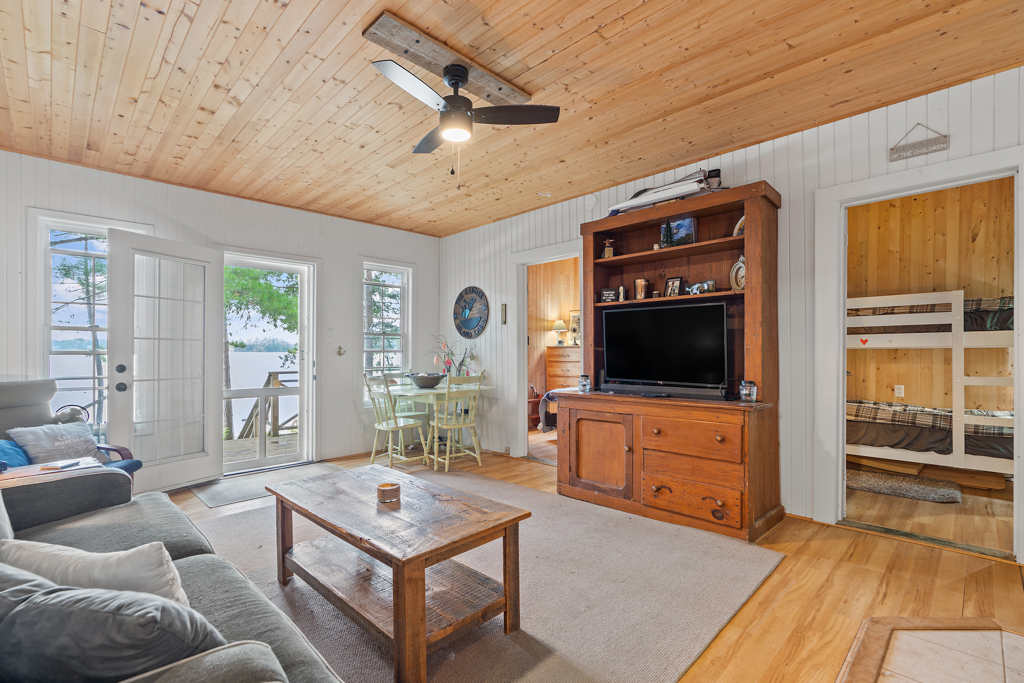 A bright, open cottage living space with a small dining table, a television, a couch, and a coffee table.