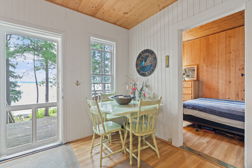 A small, light green dining table and chairs sits in the corner of a bright, open cottage living space