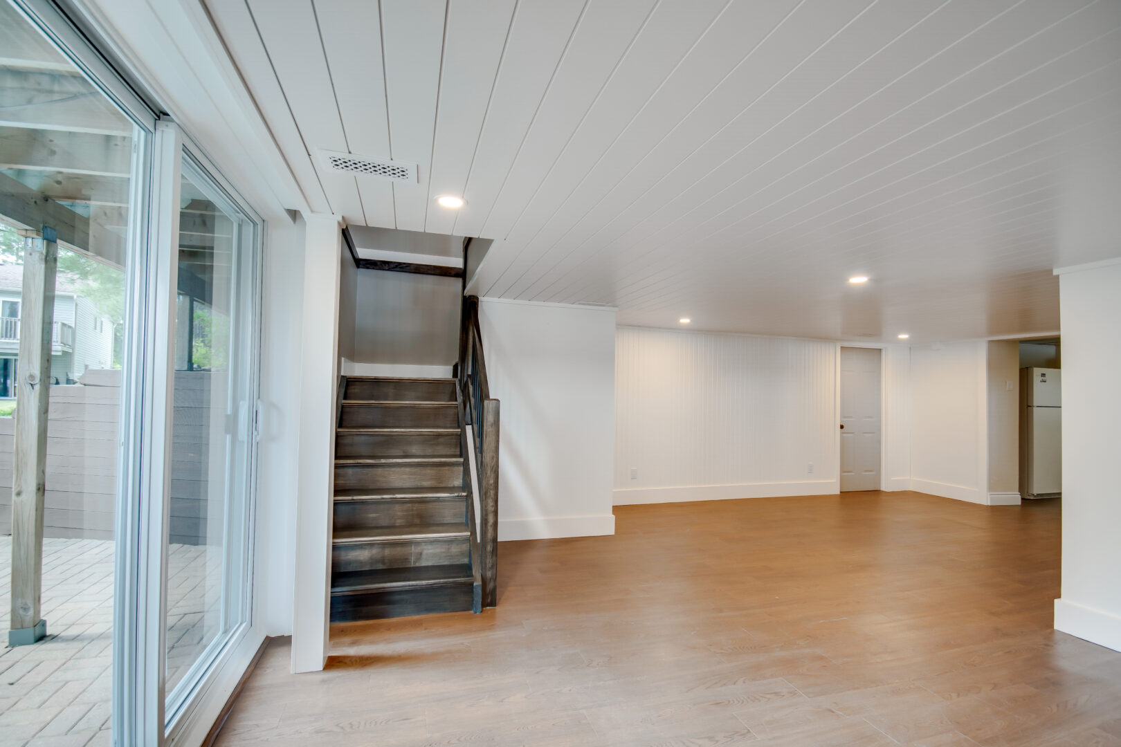 A bright, sparse lower level with hardwood flooring, stairs leading up, and double glass doors that lead to a walk-out patio.
