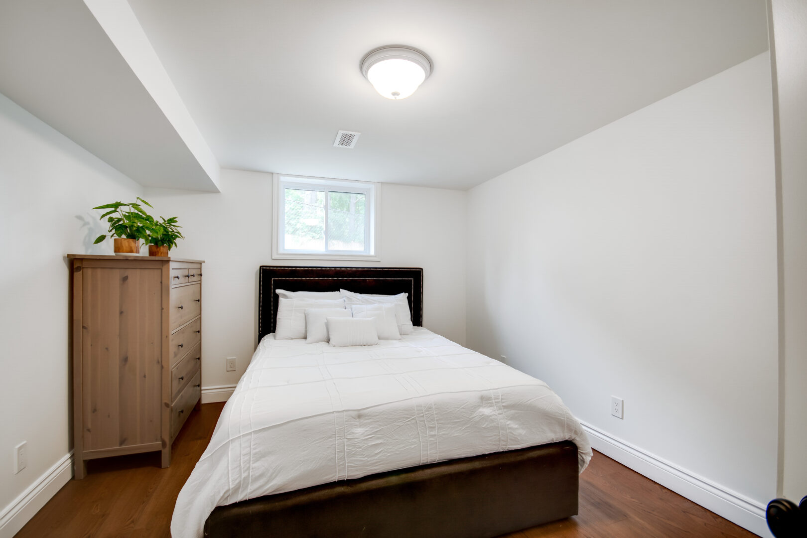 A small but bright bedroom with hardwood flooring and white bedding.