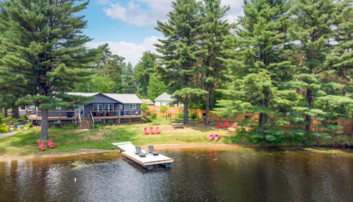 A bungalow cottage sits on a sloping grassy yard in front of a still lake.