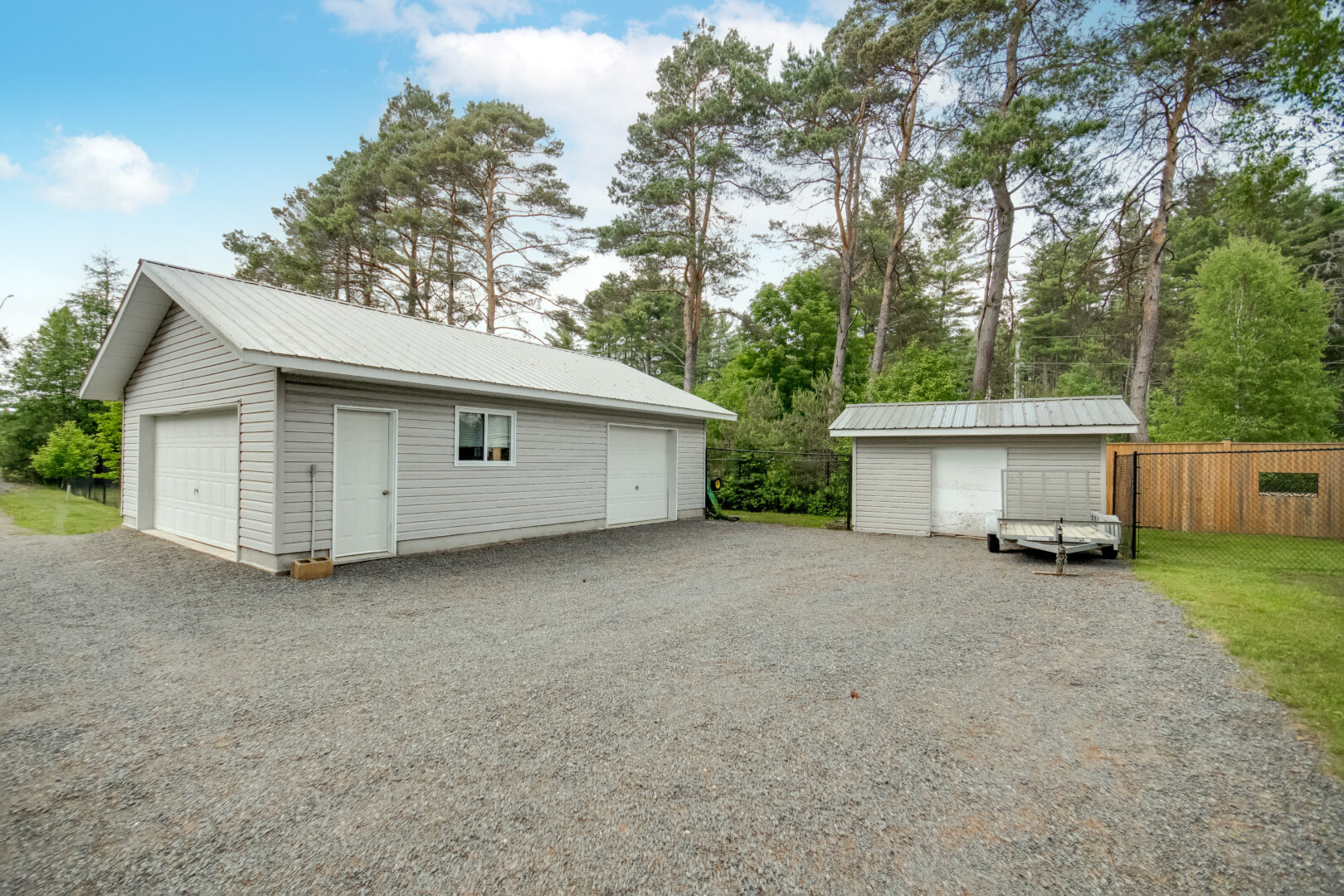 A detached garage and a small shed sit just off a large gravel driveway.