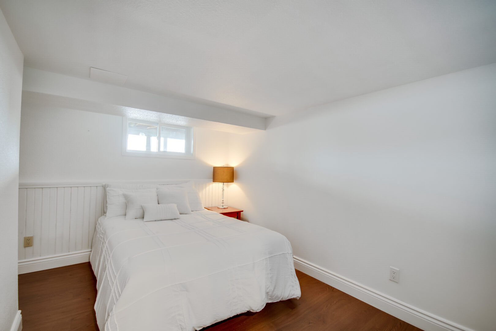 A small but bright bedroom with hardwood flooring and white bedding.