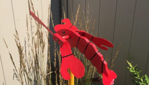 A lobster whirligig in a backyard garden