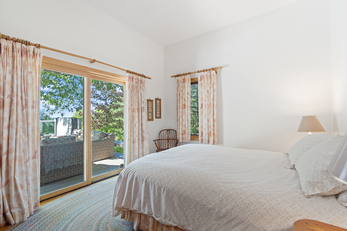A bright bedroom with a large bed and double glass doors that lead out to a back deck.