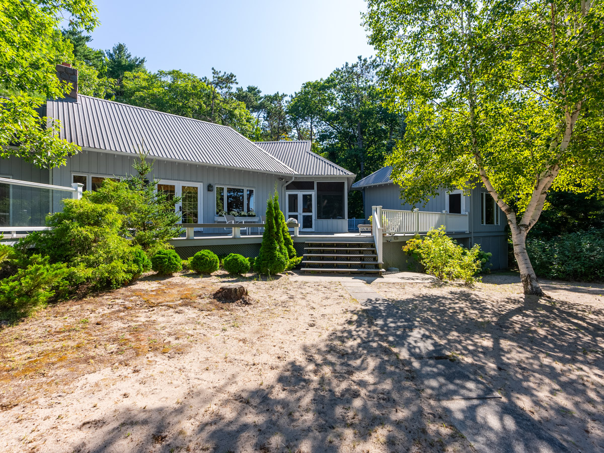A wide, sandy area lined in greenery, in front of a large luxury cottage.
