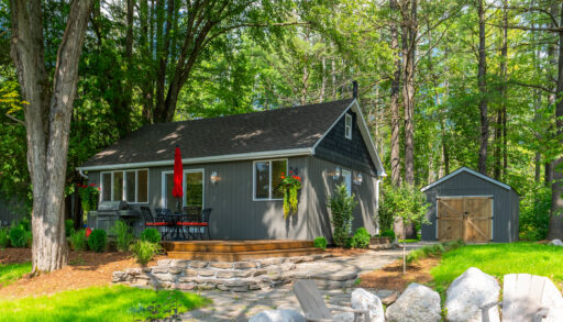 A fire pit. A cottage sits across a wide grassy yard.