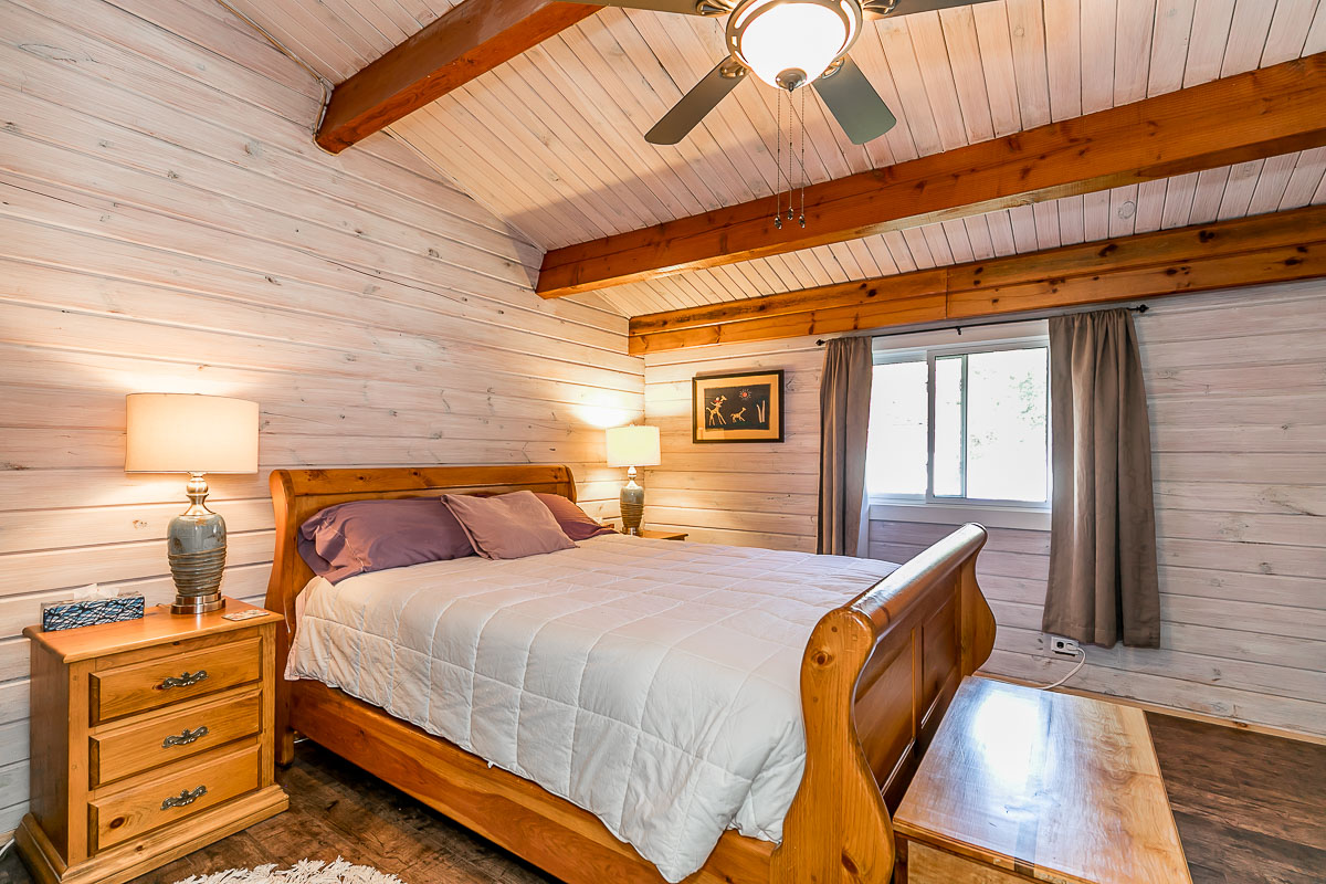 A big bedroom with a large bed and a sloping ceiling that has exposed beams.