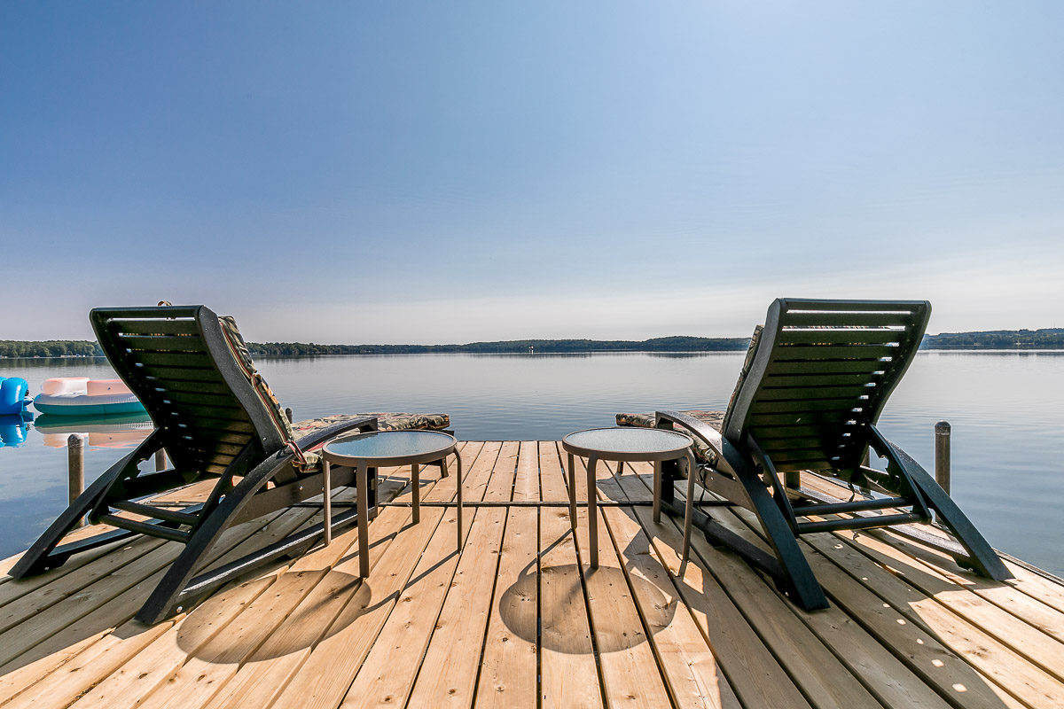 Two chairs sit on a dock, looking out over a lake.