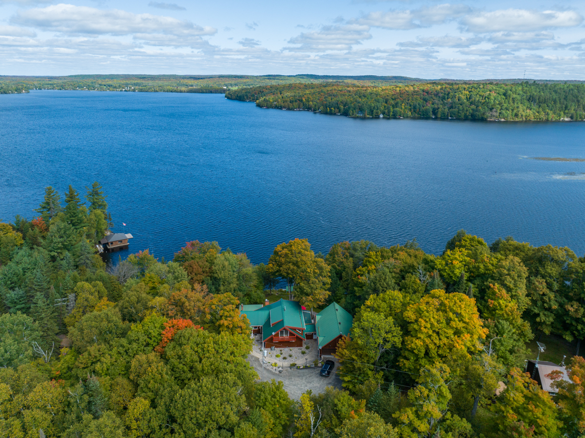 Overhead view of a cottage surrounded by trees, in front of a lake.
