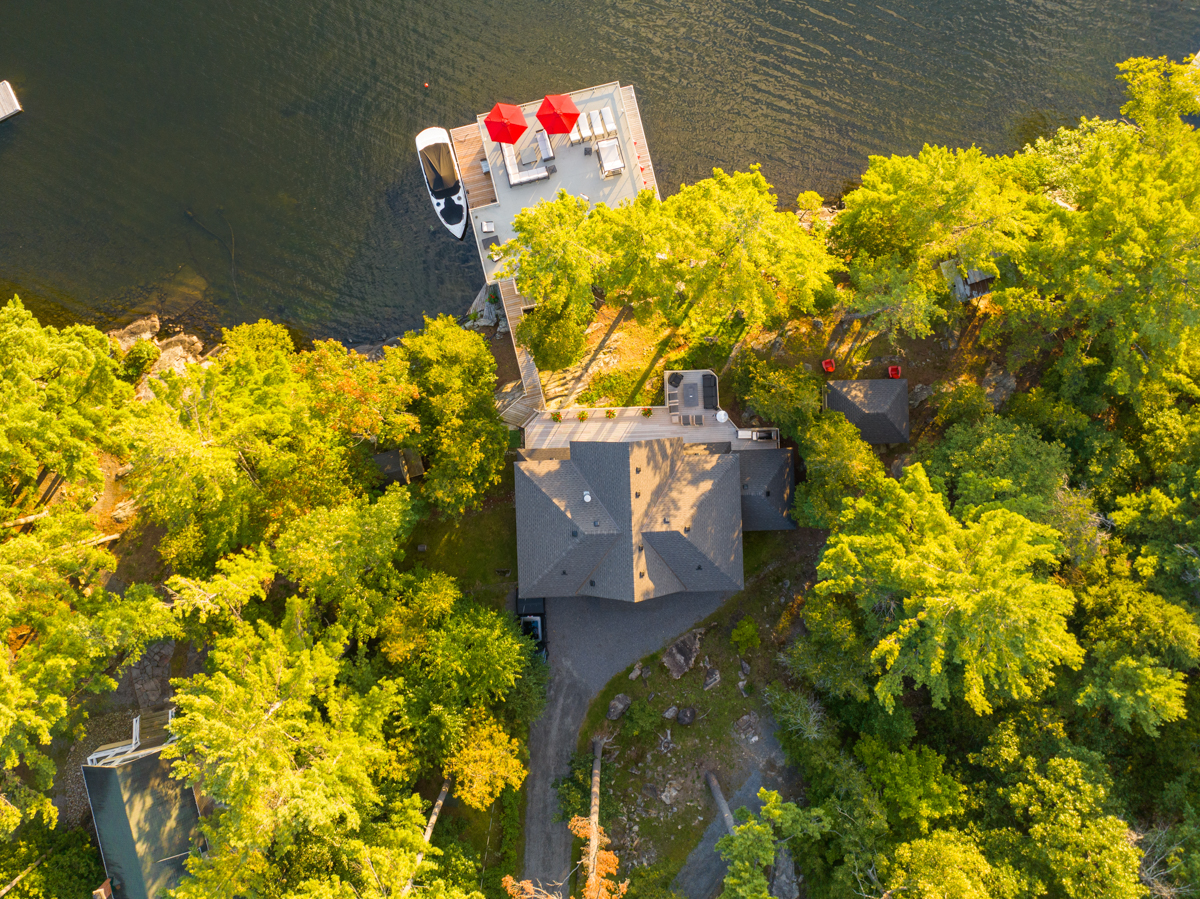 Overhead view of a large lakeside cottage surrounded by green trees.