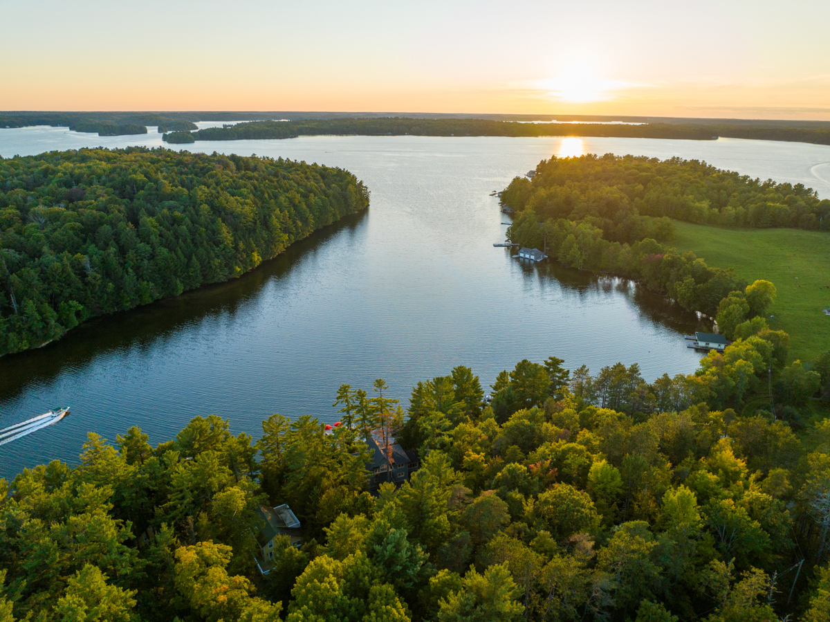 A sunset view looking out over a lake with trees on either side.