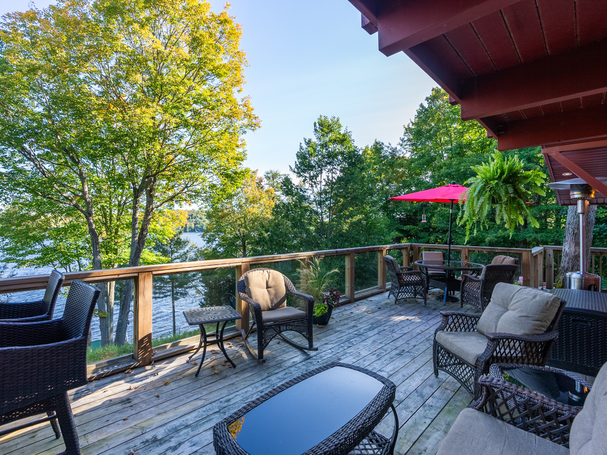 A deck with lots of outdoor furniture extends off the back of a cottage.