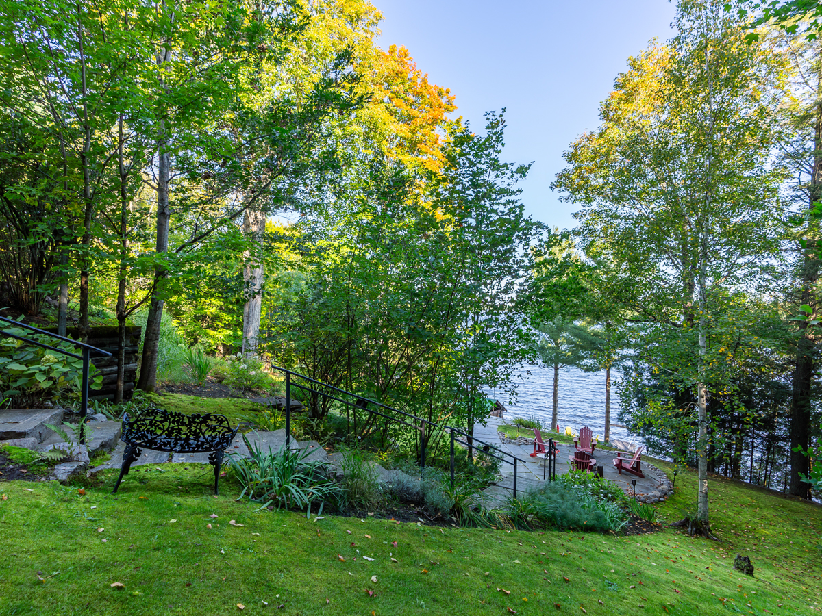 Steps leading down a grassy hill toward a lake. There is a landing halfway down with a fire pit area.