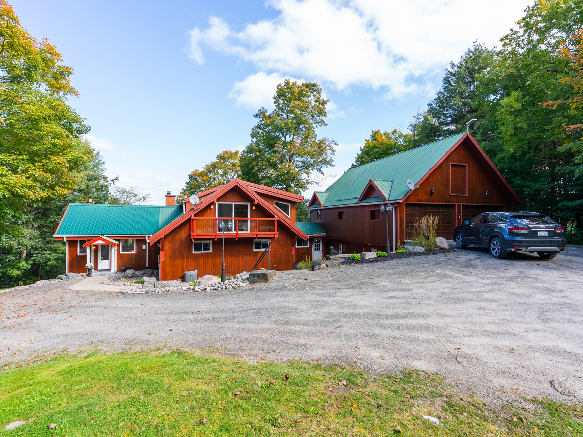 A large cottage with a garage, a big driveway, and a green roof.