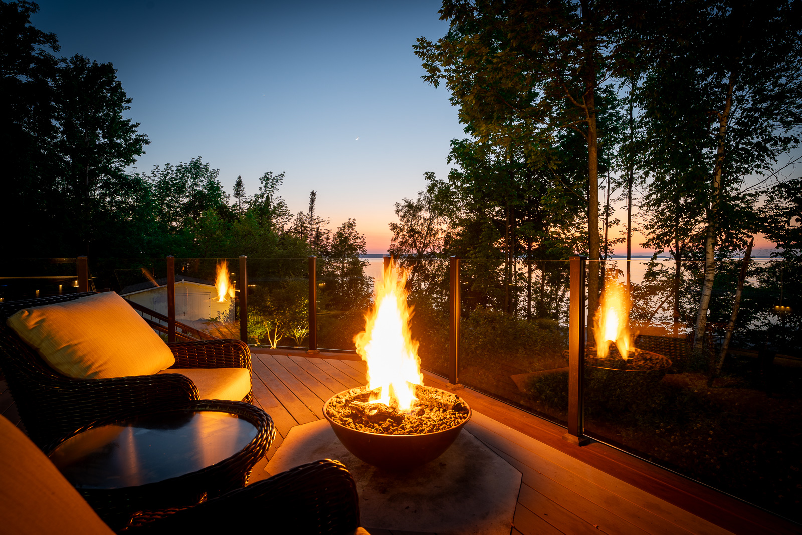 A fire bowl glowing at night, on a deck overlooking a lake.