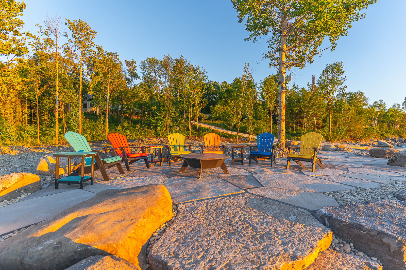 A large patio with a fire table, surrounded by colourful Muskoka chairs.