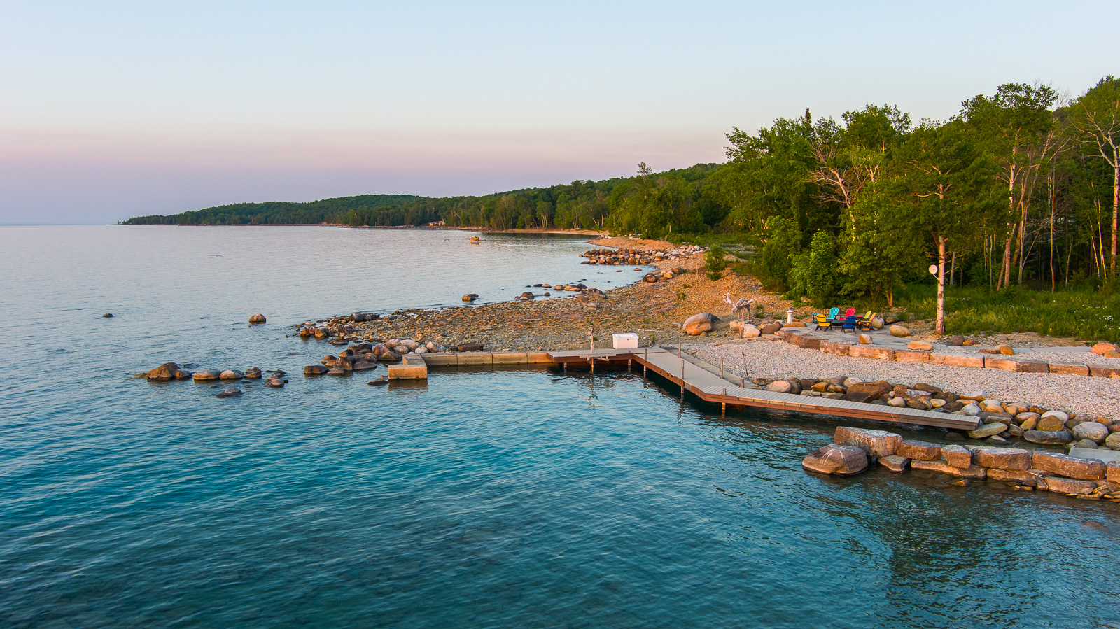 A large patio with colourful Muskoka chairs and a dock, on a quiet stretch of lake.