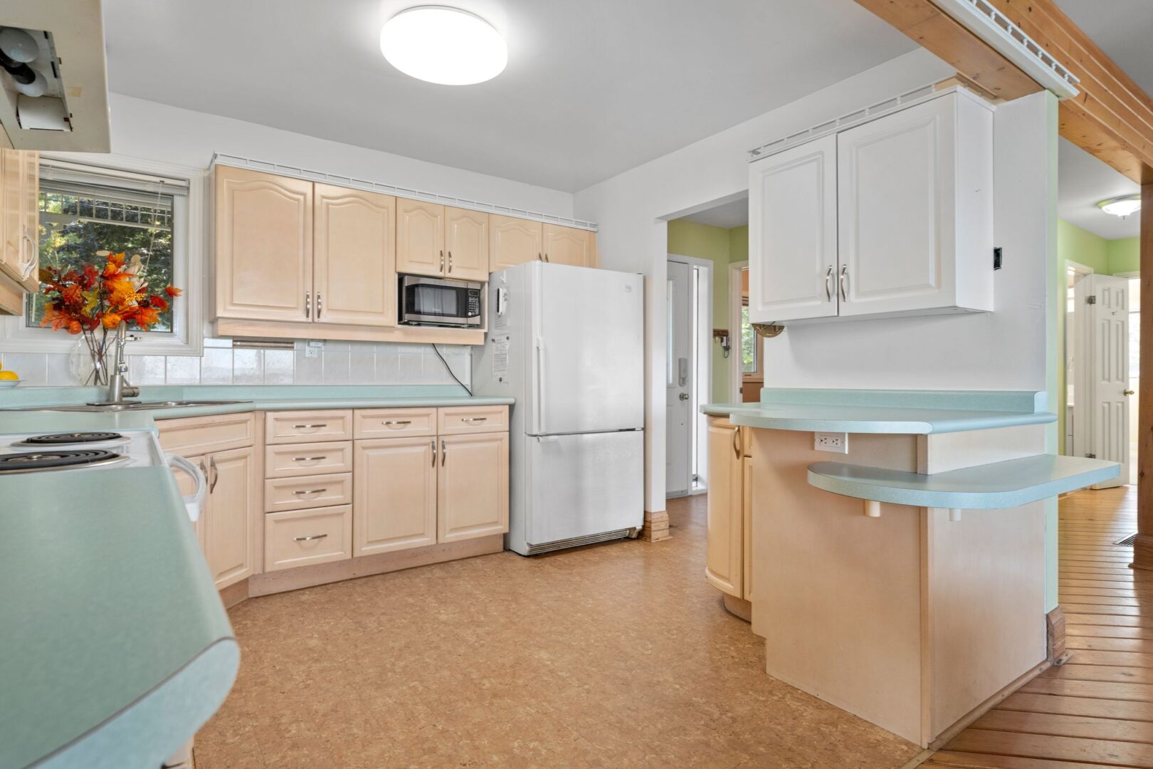A kitchen with light green countertops, beige cabinets, and white appliances.