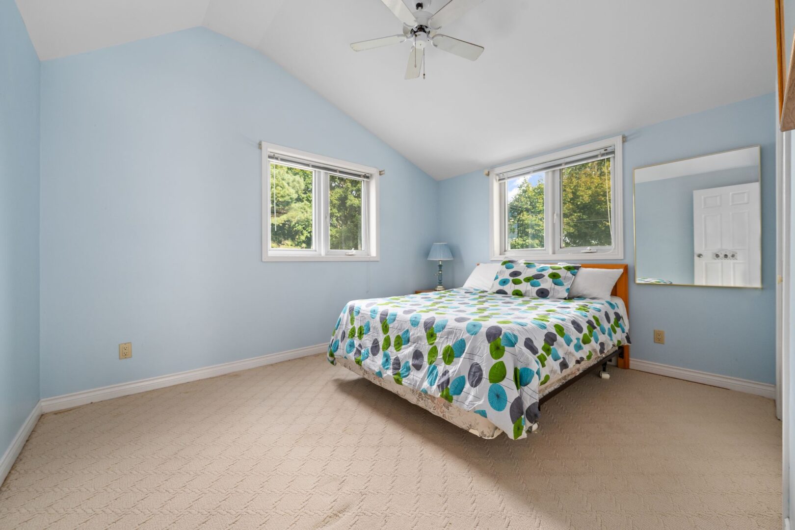 A large bedroom with light blue walls, a sloping ceiling, and a bed.