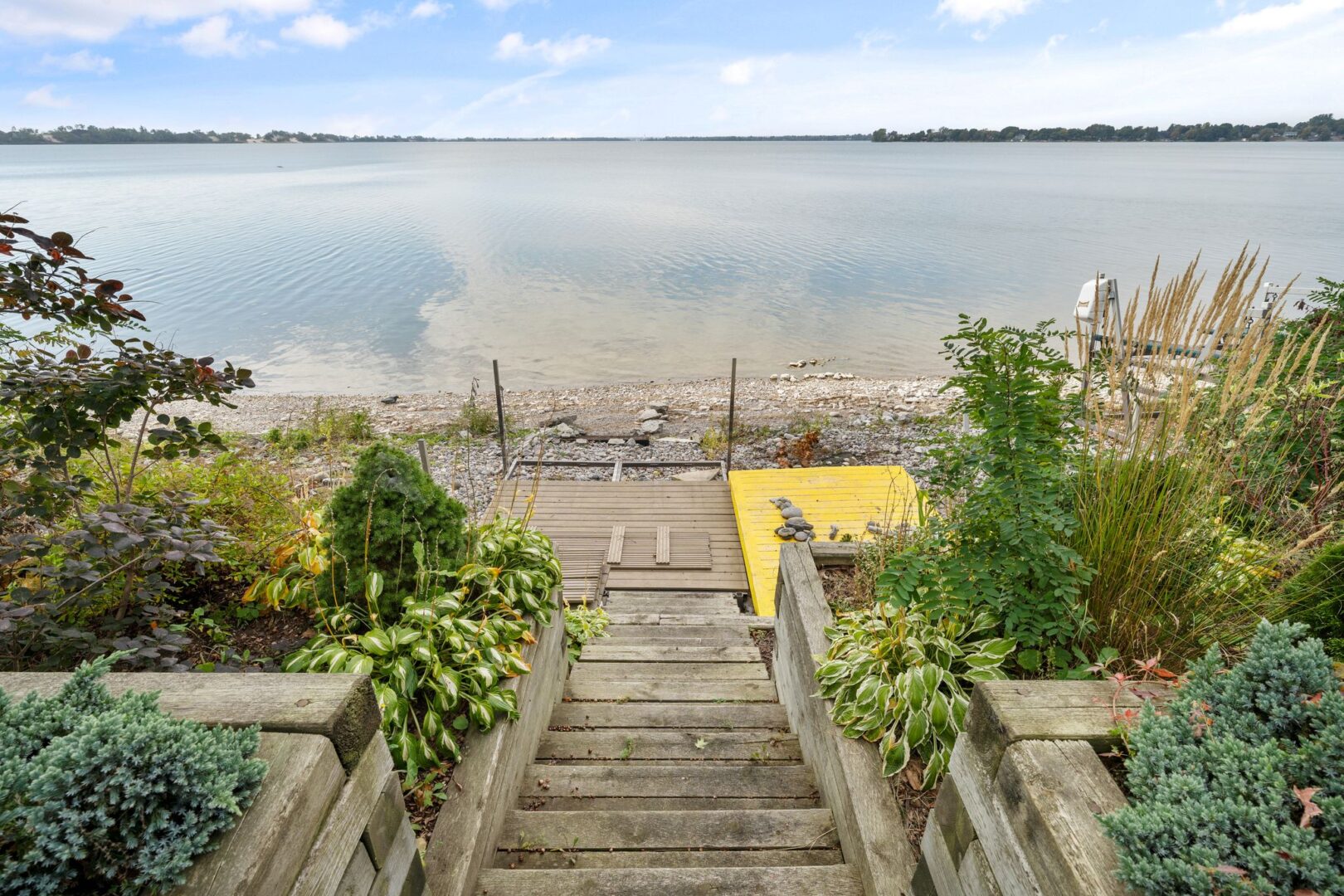 Wooden steps lead down to a dock on the rocky shoreline of a lake.