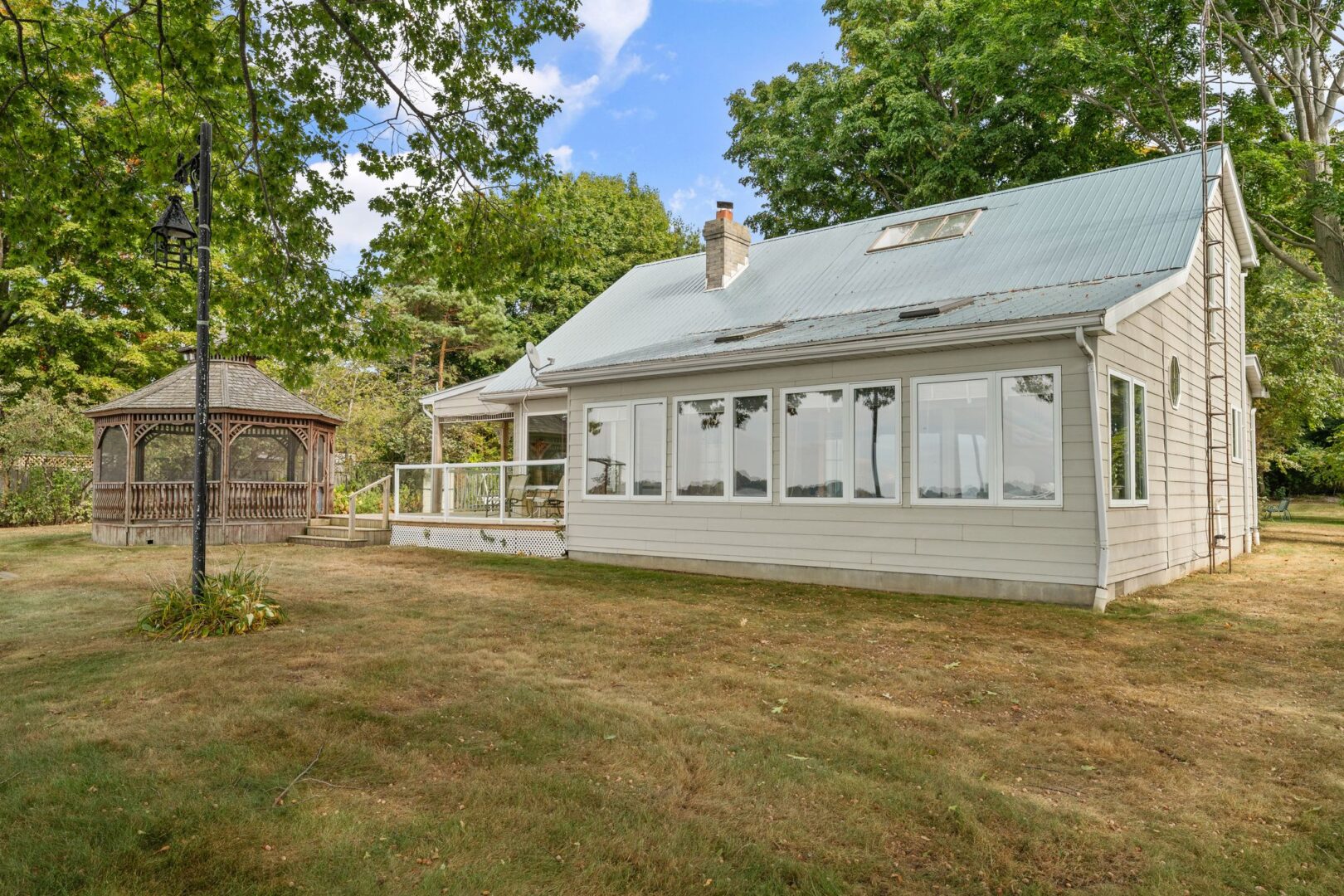 The back of a cottage property with a big sunroom, a deck, and a gazebo.