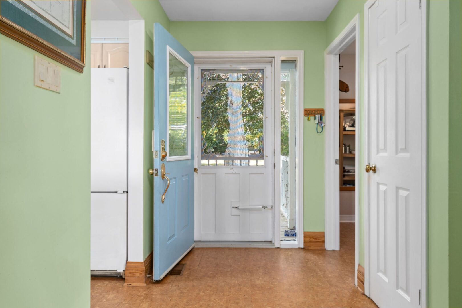 Inside the front entrance of a bright cottage with hardwood floors and a screen door.