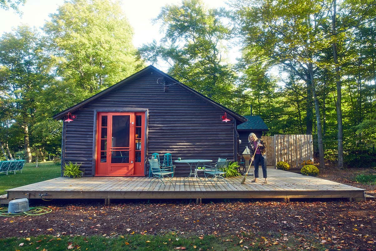 a woman sweeps leaves off of her cottage deck
