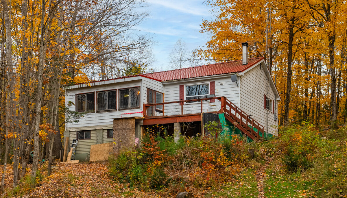 A small white cottage with red railings and a red roof, sitting at the top of a grassy hill.