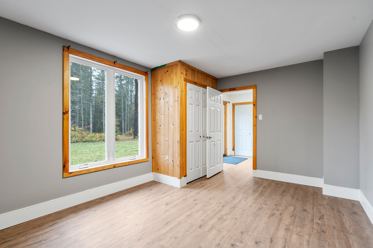 A large, empty bedroom with grey painted walls, a big window, and a closet.