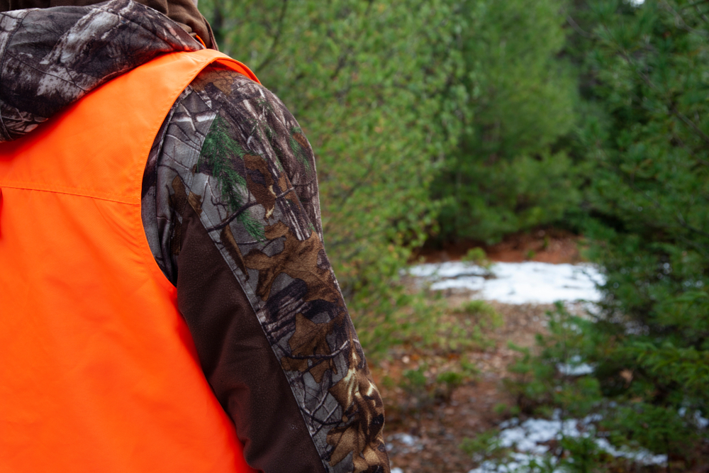 man wearing hunter orange vest in the woods