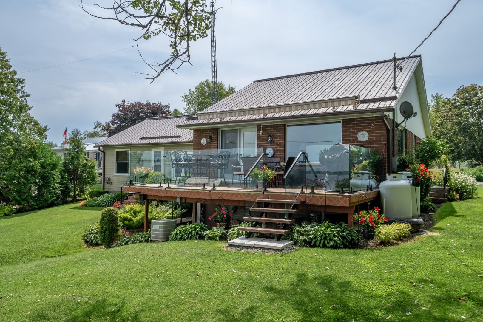 The back of a waterfront bungalow on a grassy lot. A large deck with a glass railing extends off the back of the home.