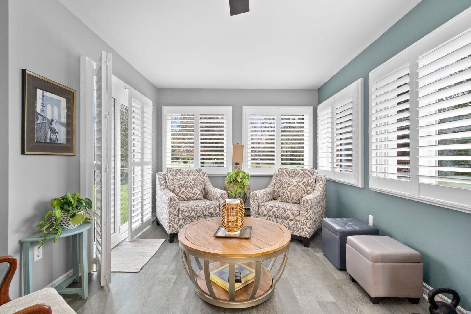 A bright sitting area with chairs, big windows, double doors leading out to a patio, and grey vinyl plank flooring.