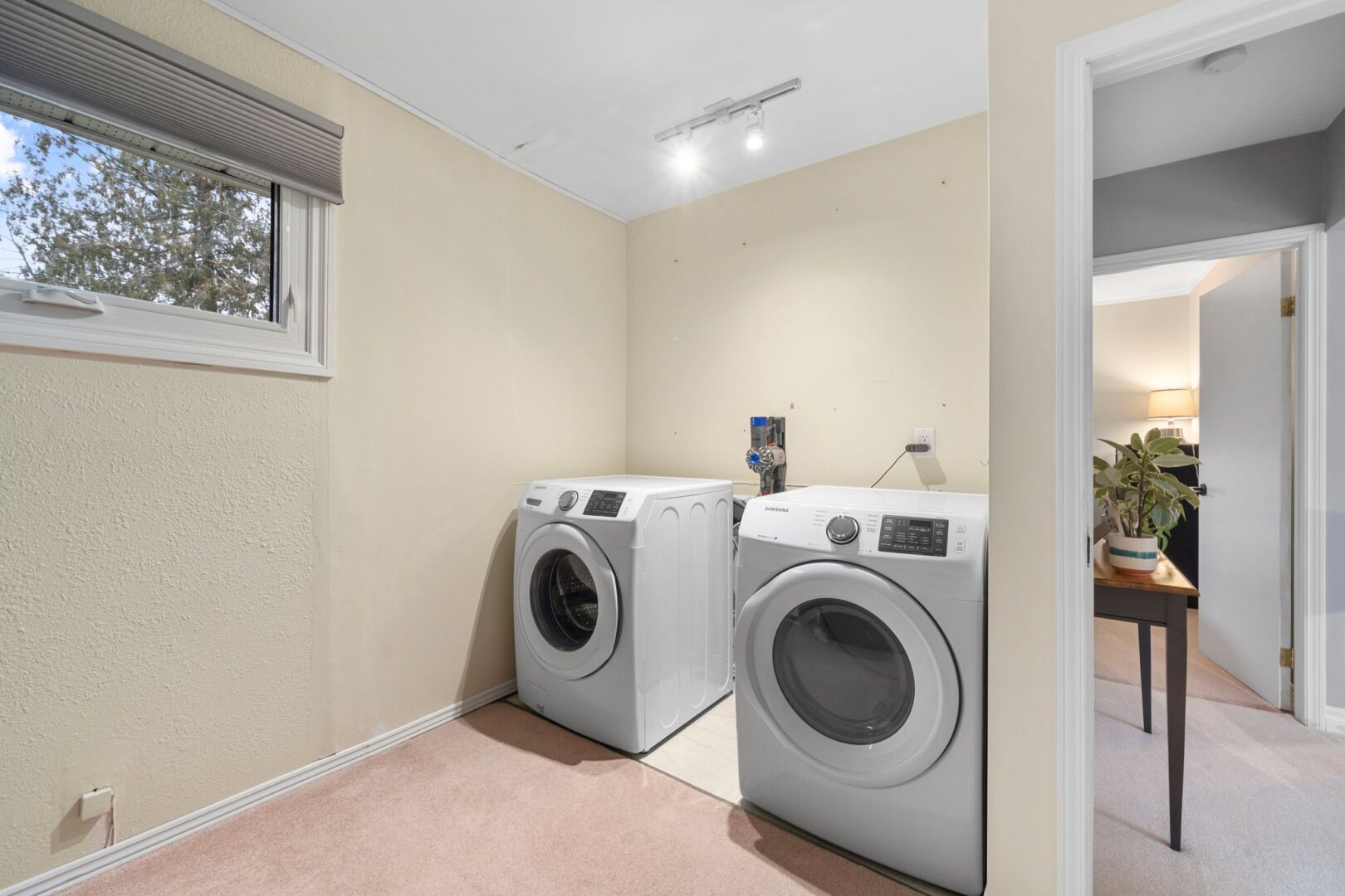 A laundry area with a washing machine, a dryer, and a light pink carpet.