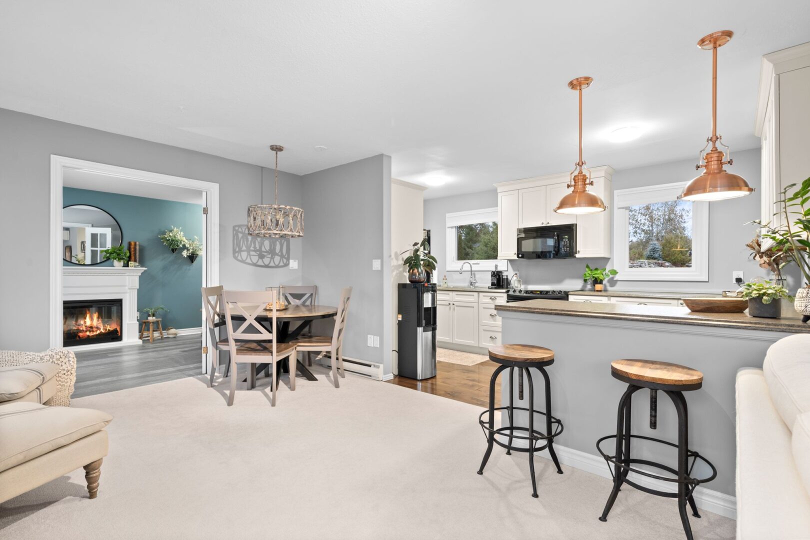 A bright, open area that flows between a dining area, a living room, and a kitchen. Barstools sit tucked into a kitchen peninsula.