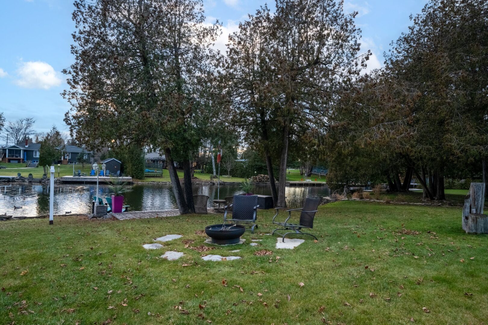 A small fire pit sits on a grassy yard, just off the edge of a river.