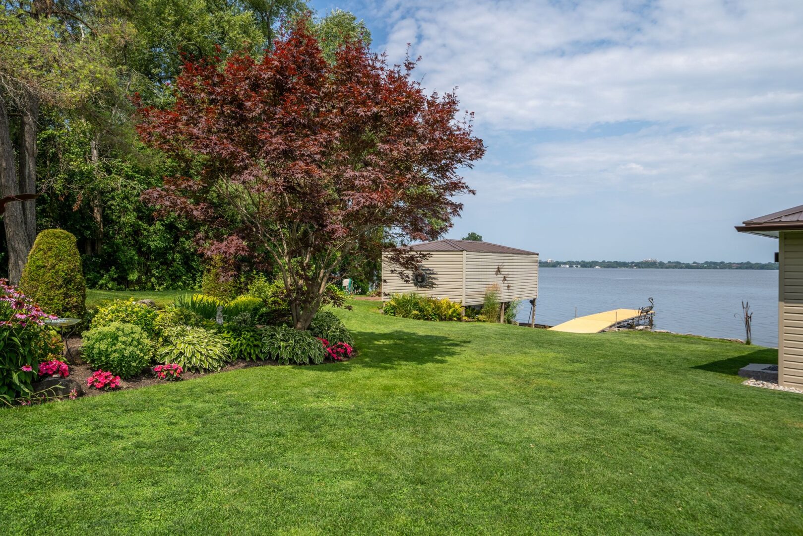 A large, open grassy lot slopes down to the waterfront. A small boat launch and a dock sit at the shoreline.